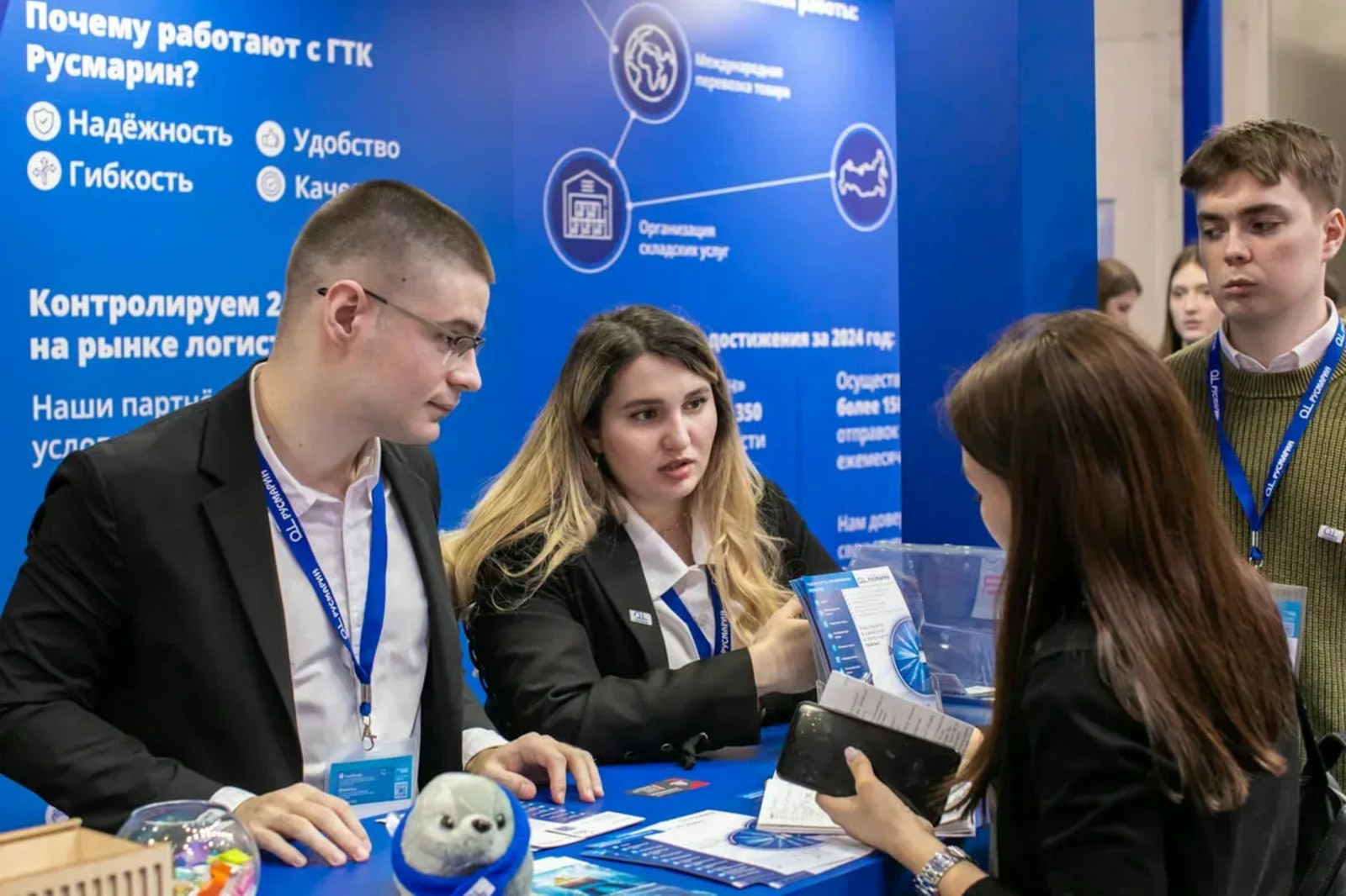 Two exhibitors talking with a visitor across a branded booth counter at a business exhibition
