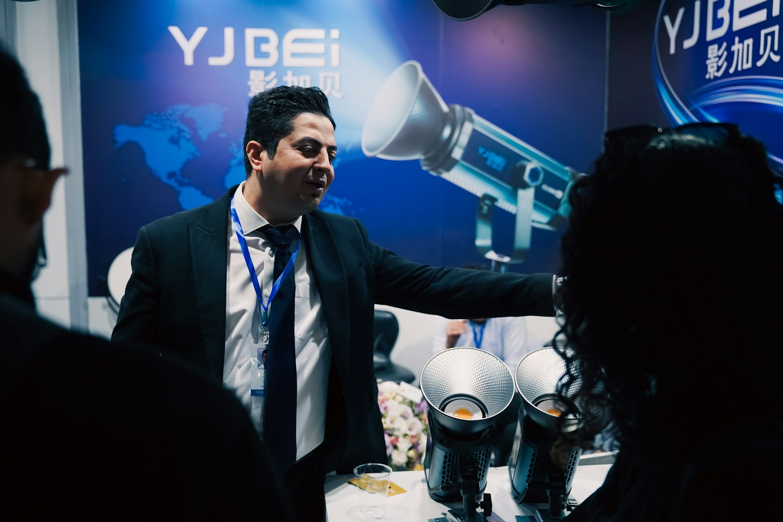 An exhibitor in a lanyard showing a product to a visitor at a trade show booth