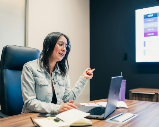A host presenting a live webinar from a desk, speaking to a laptop with a presentation on screen