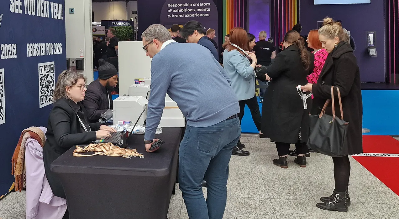 Event staff working at a registration counter with a laptop and a badge printer while attendees queue alongside