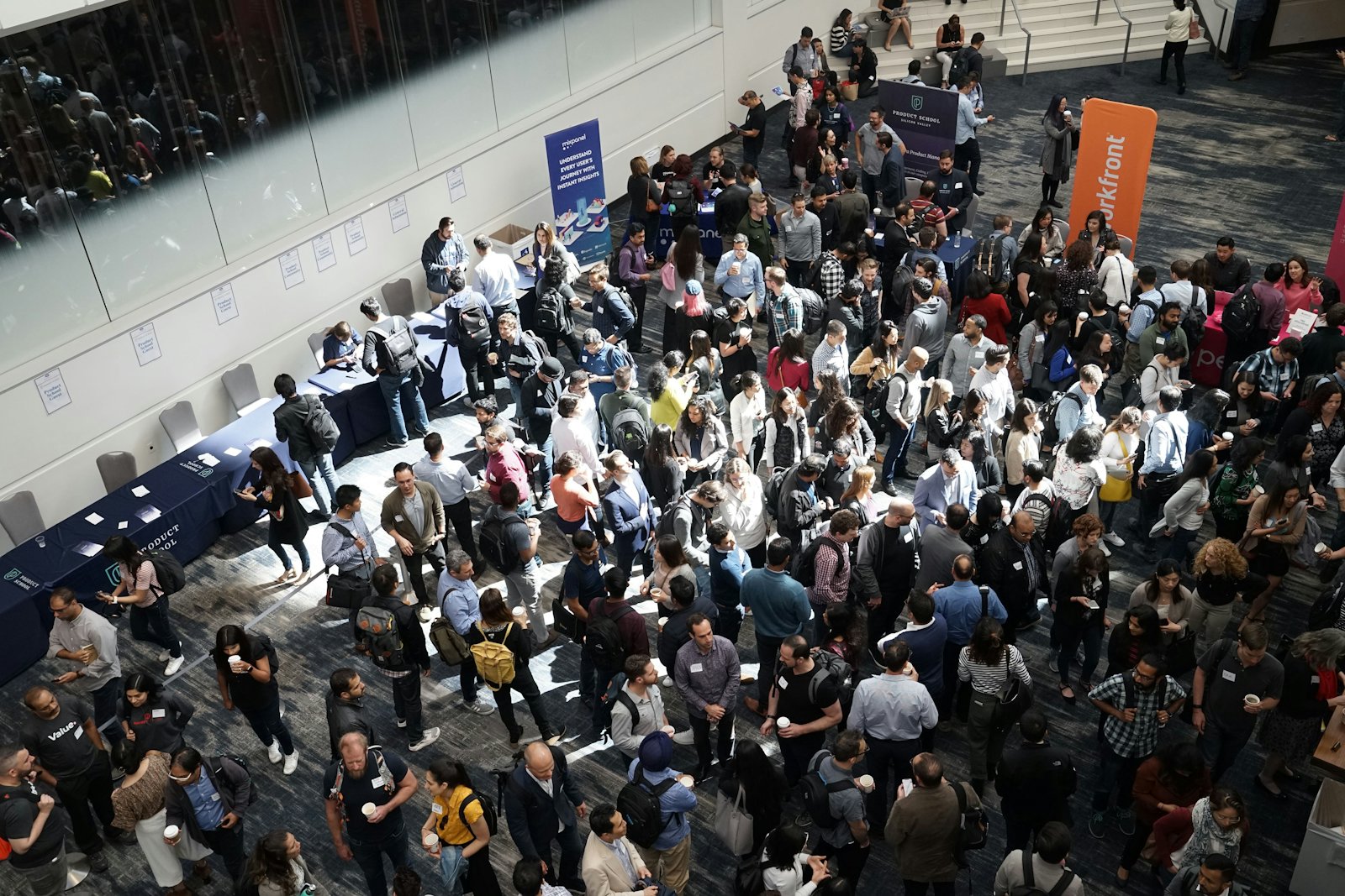 A conference foyer seen from above, filled with several hundred attendees gathered between exhibition stands