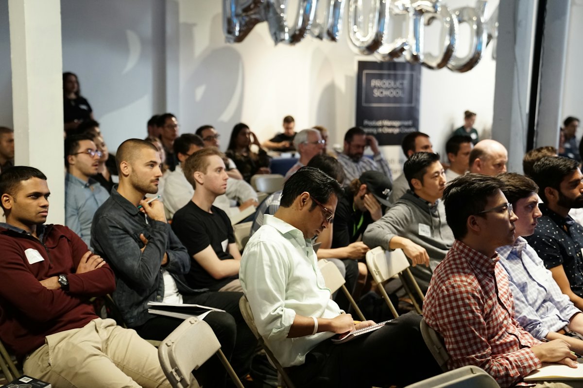 Rows of seated attendees wearing name badges, listening during a conference session